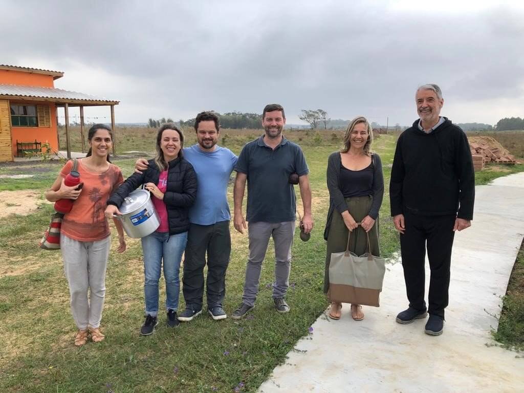 Seis pessoas estão de pé sorrindo para a foto, sendo três praticantes mulheres e três homens, incluindo-se o lama Padma Samten, à direita. Ao fundo pode-se avistar as dependências do CEBB Akanishta, à esquerda e um céu amplo ao fundo